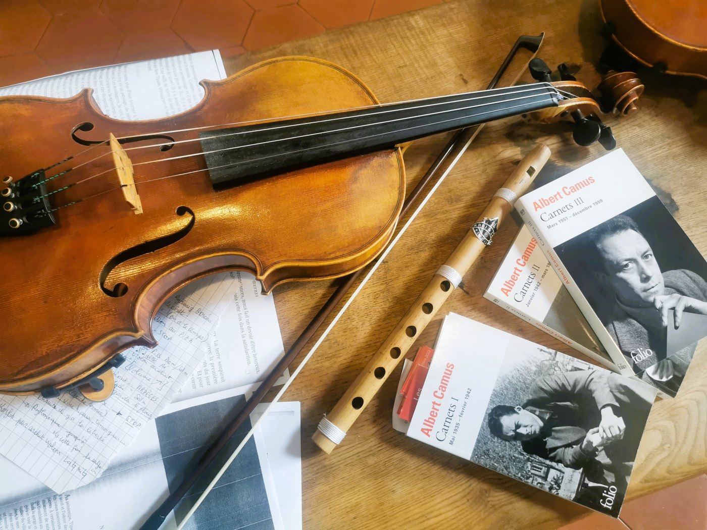 Un violon, un archet, une flûte et les trois volumes des Carnets d'Albert Camus posés sur une table