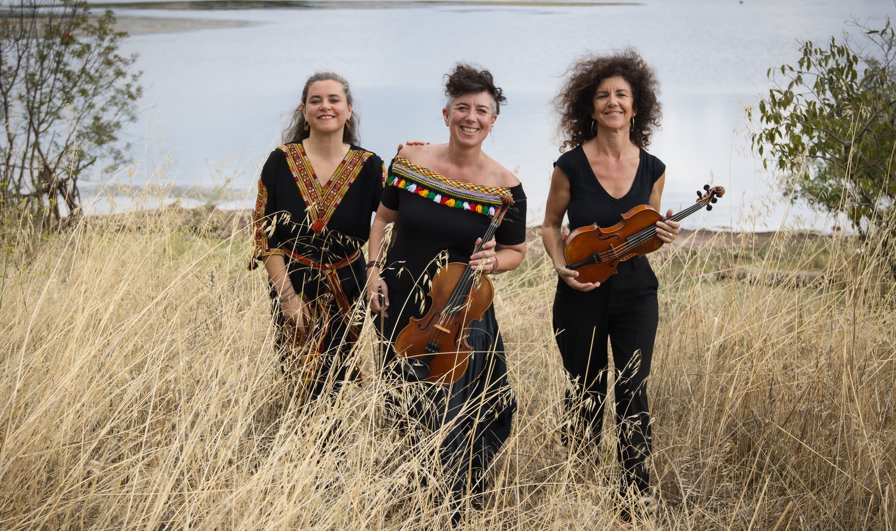 Eglantine Jouve, Delphine Chomel et Marion Diaques dans les hautes herbes sèches, au bord de l'eau, violons à la main