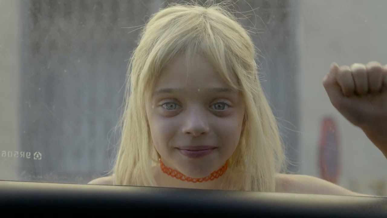 Une petite fille blonde derrière une vitre, dans le clip Fol