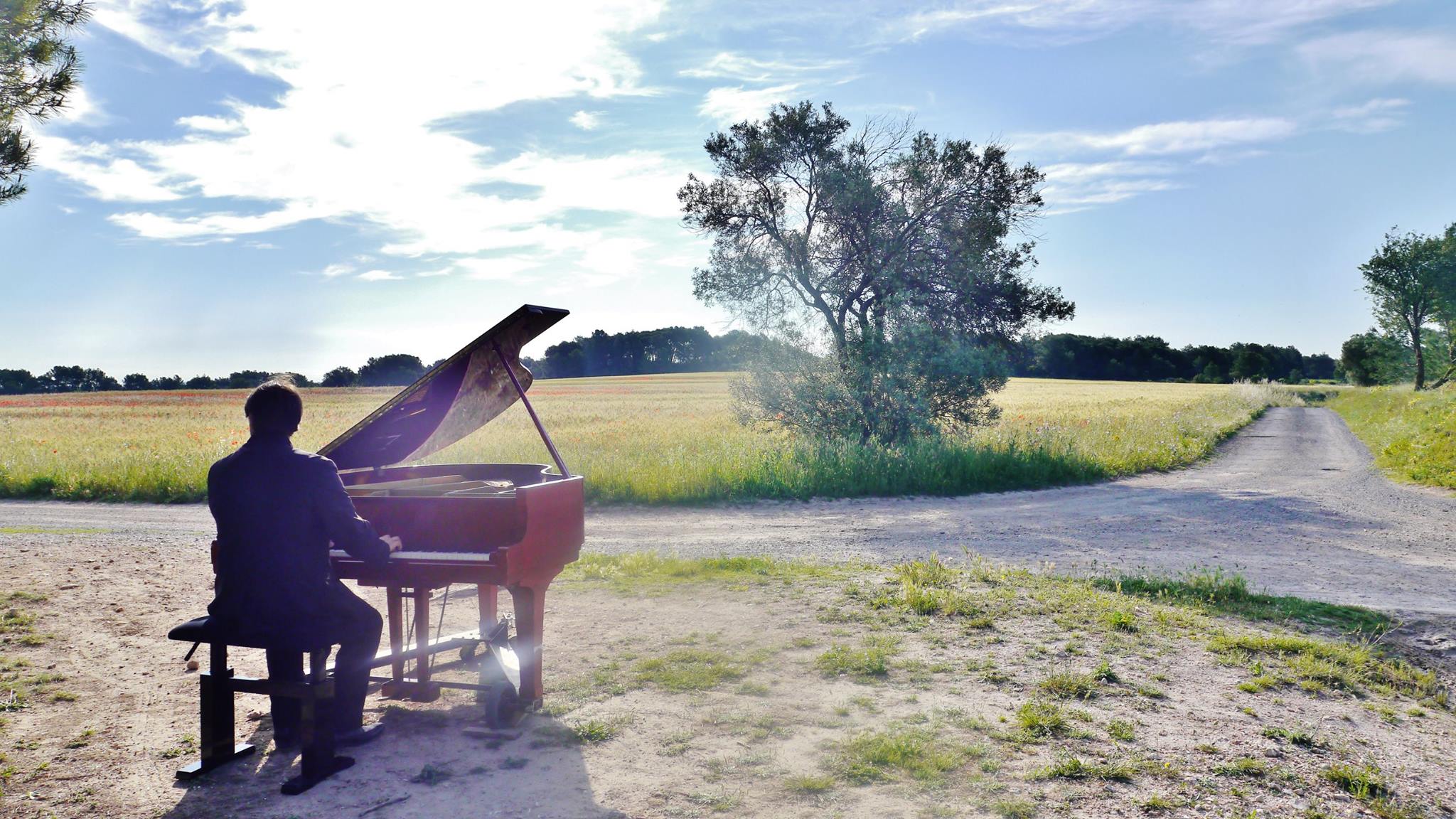 Le piano rouge posé à la croisée de deux chemins, face aux champs de coquelicots